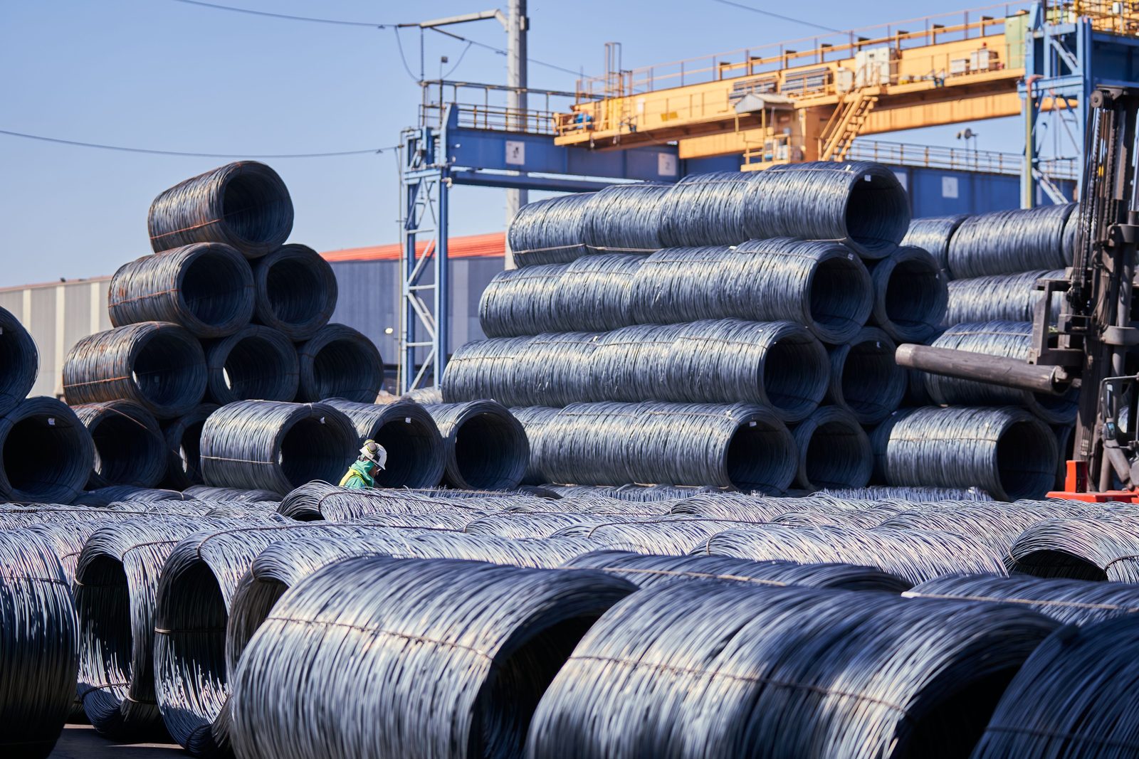 Steel wire coils stacked in tiers in an outdoor stockyard with an overhead crane above them