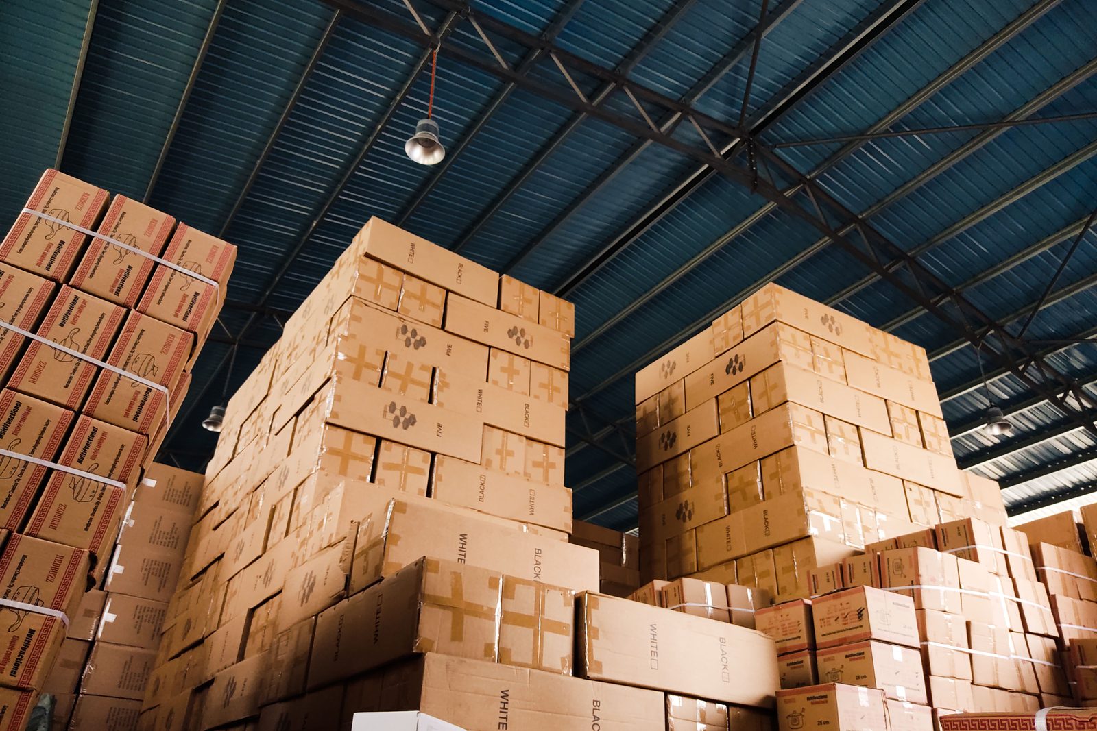 Cardboard boxes stacked high in tiers inside a small warehouse